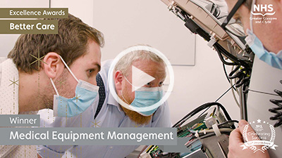 Three men, wearing surgical masks, looking at a medical device