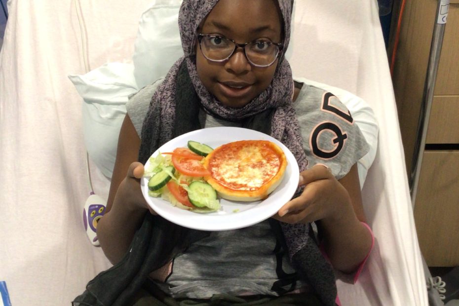 Girl saitting on hospital bed holding plate with pizza and salad