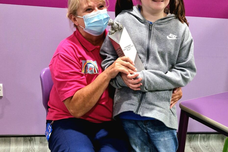 Teri, sitting while Emily holds the Health-Related Play Award. They are in the Royal Hospital for Children