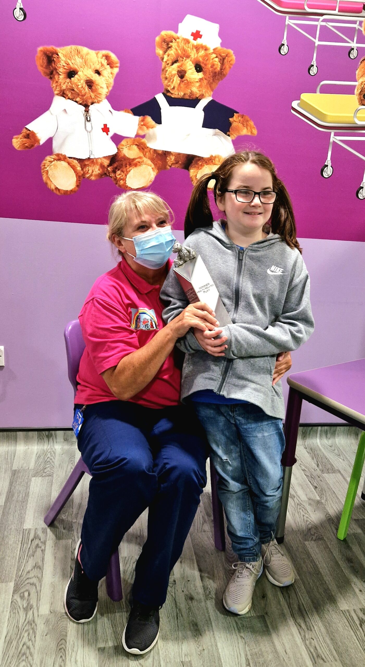 Teri, sitting while Emily holds the Health-Related Play Award. They are in the Royal Hospital for Children