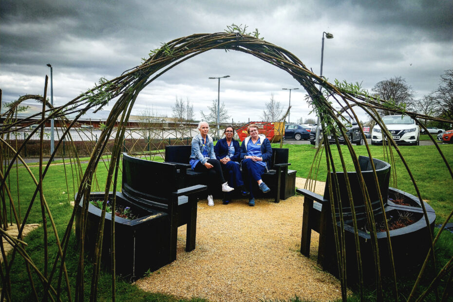 Three members of staff seated within the new Willow Arch surrounded by hospital grounds and under a cloudy sky