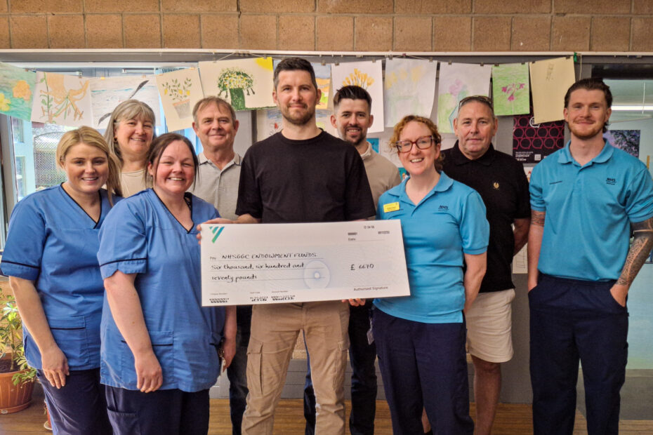 Scott Gold in centre of picture, holding cheque to be presented to staff at the NRU. From left: staff nurse Lauren McAndrew, Mechelle Gold, charge nurse Hazel Elliott, Kenny Gold, Scott Gold, Ian Gold, AHP Team Lead Donna Bisland, Mick Marlin, physiotherapist Jack McGeachin. Image: NHSGGC
