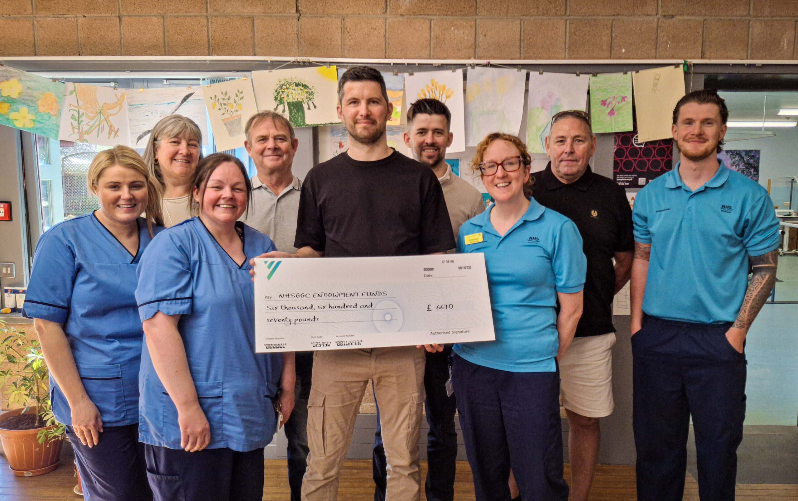 Scott Gold in centre of picture, holding cheque to be presented to staff at the NRU. From left: staff nurse Lauren McAndrew, Mechelle Gold, charge nurse Hazel Elliott, Kenny Gold, Scott Gold, Ian Gold, AHP Team Lead Donna Bisland, Mick Marlin, physiotherapist Jack McGeachin. Image: NHSGGC