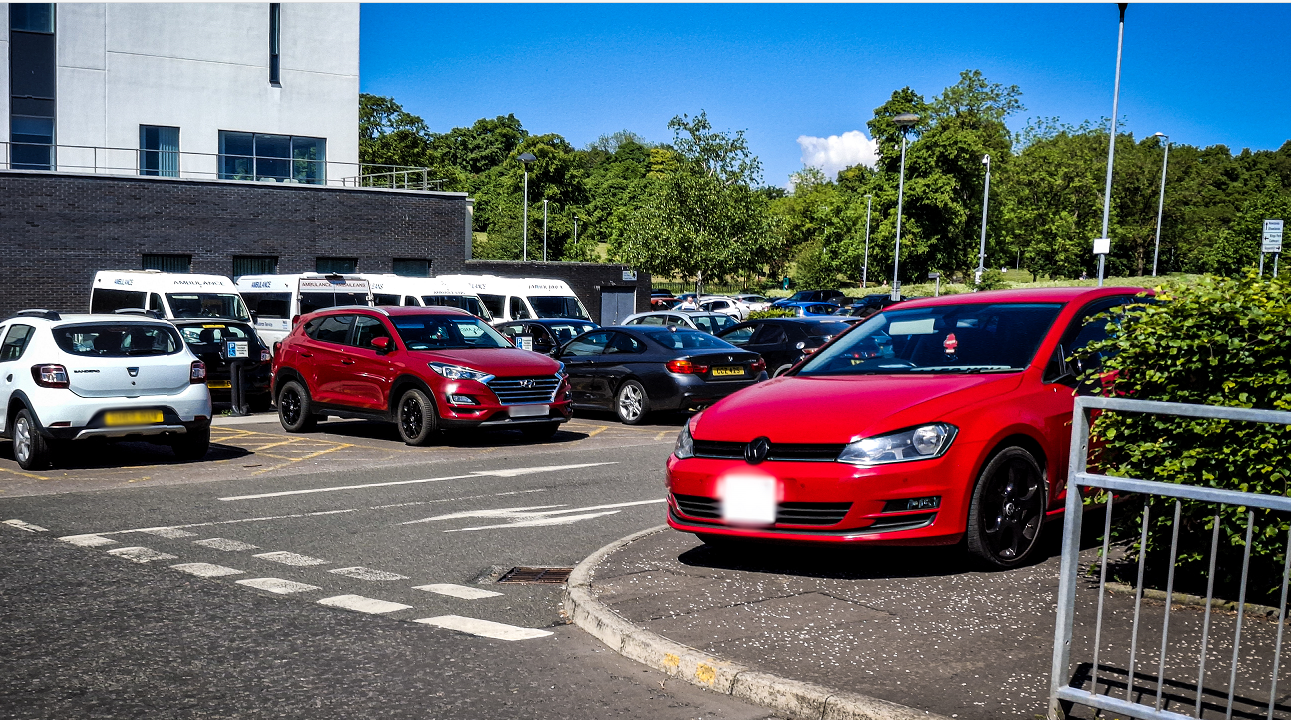 Cars parked outside the New Victoria Hospital, with one red car parked on a pavement.