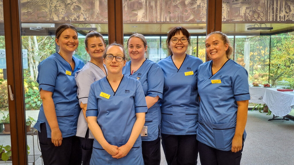 Six newly qualified nurses stand together at with the Spinal Unit garden room in the background.