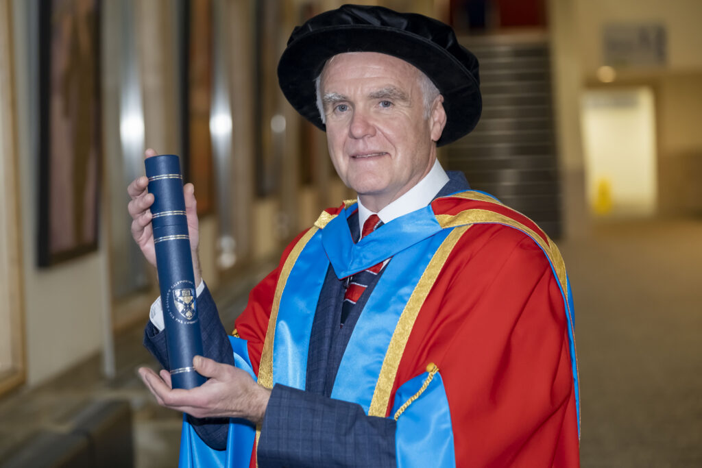 Professor Tom Steele in his graduation gown and holding his degree scroll after receiving an honorary degree from Glasgow Caledonian University.