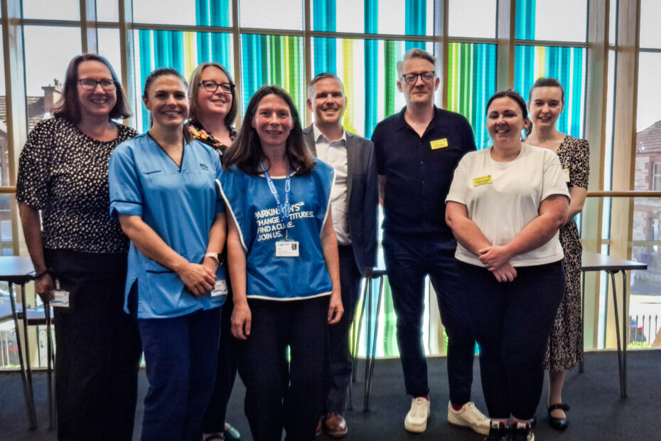 The NHSGGC team and support staff at pose for a picture in front of a coloured window.