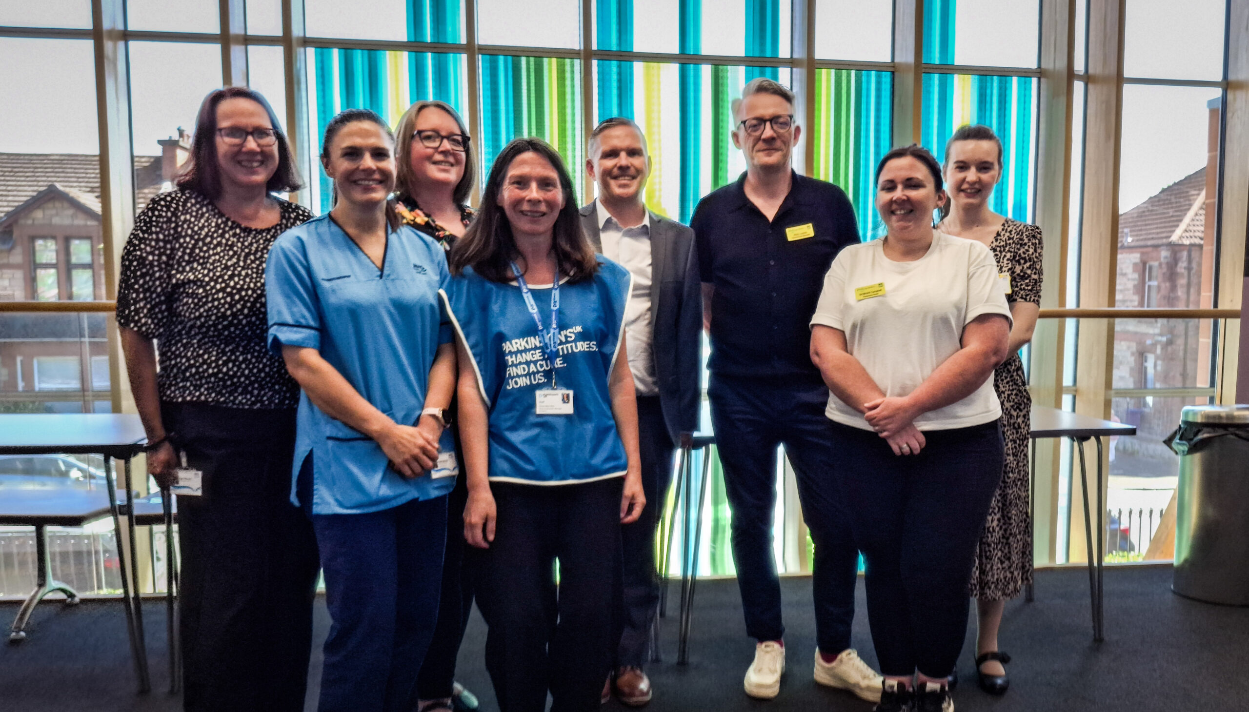 The NHSGGC team and support staff at pose for a picture in front of a coloured window.