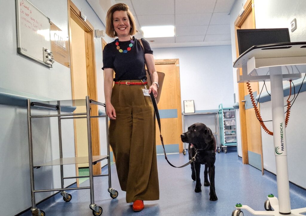 Dr Helen Grote walks down a corridor, with Cooper walking on a lead beside her.