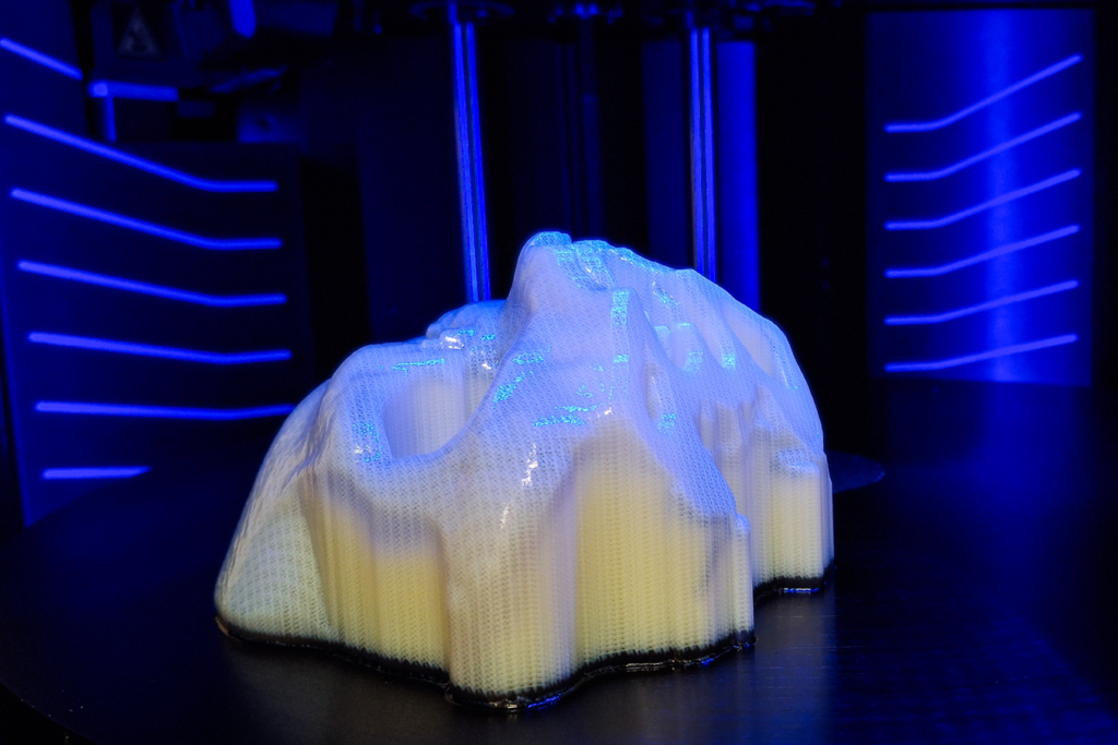 A 3D printed section of skull, bathed in blue light, inside the 3D printer with blue lit panels behind.