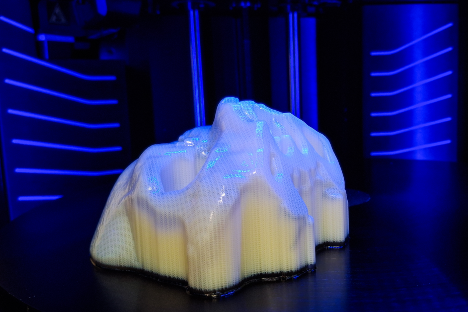 A 3D printed section of skull, bathed in blue light, inside the 3D printer with blue lit panels behind.