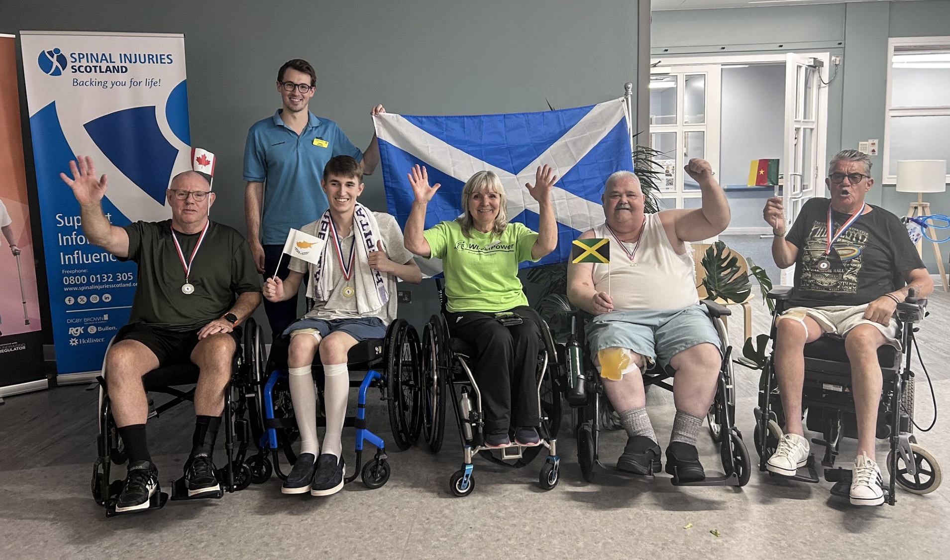 A line-up of patients and volunteers, with a Saltire in the background and each patient holding a flag from the competing countries