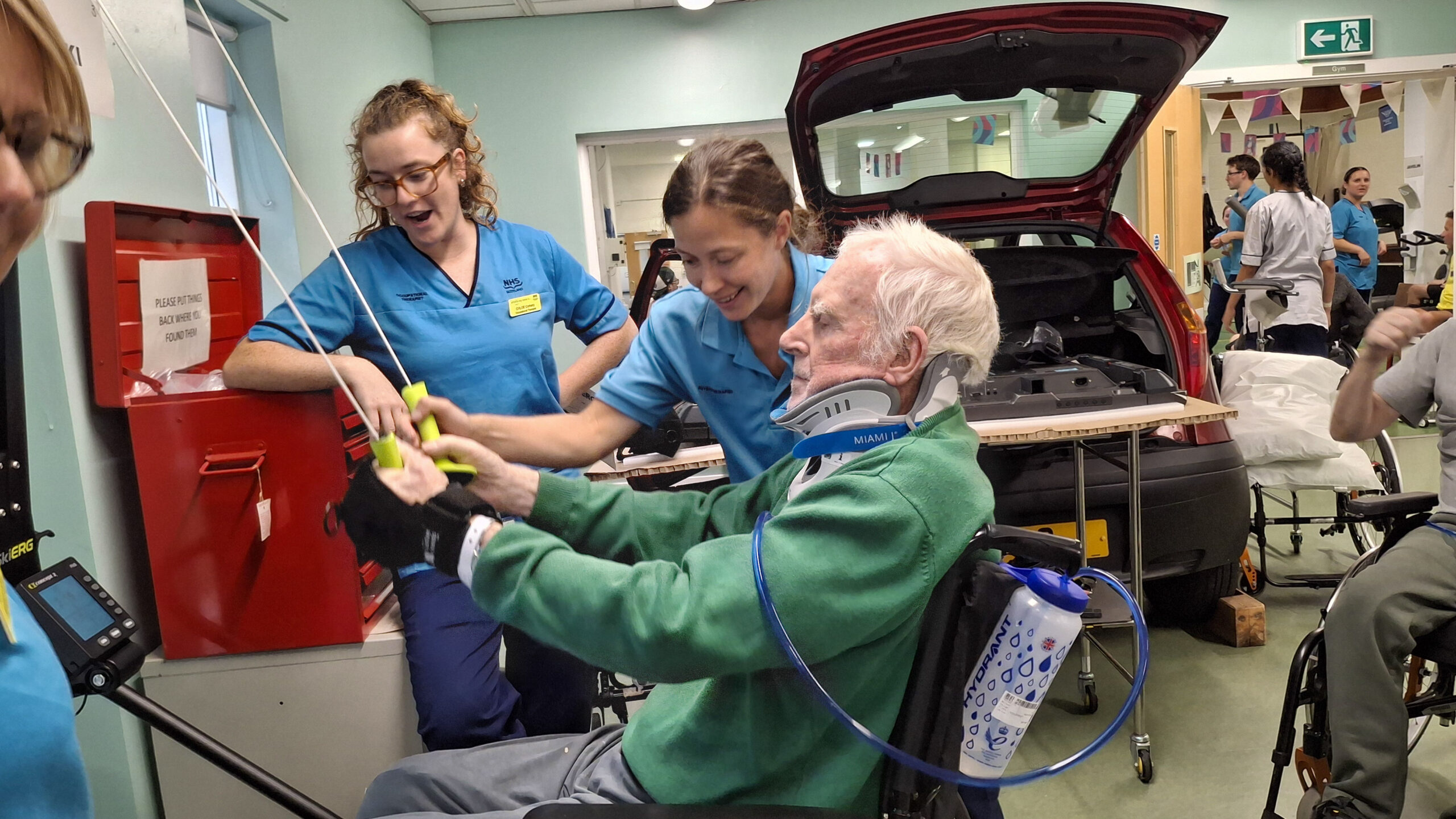 A patient takes part in weightlifting, helped by two staff members