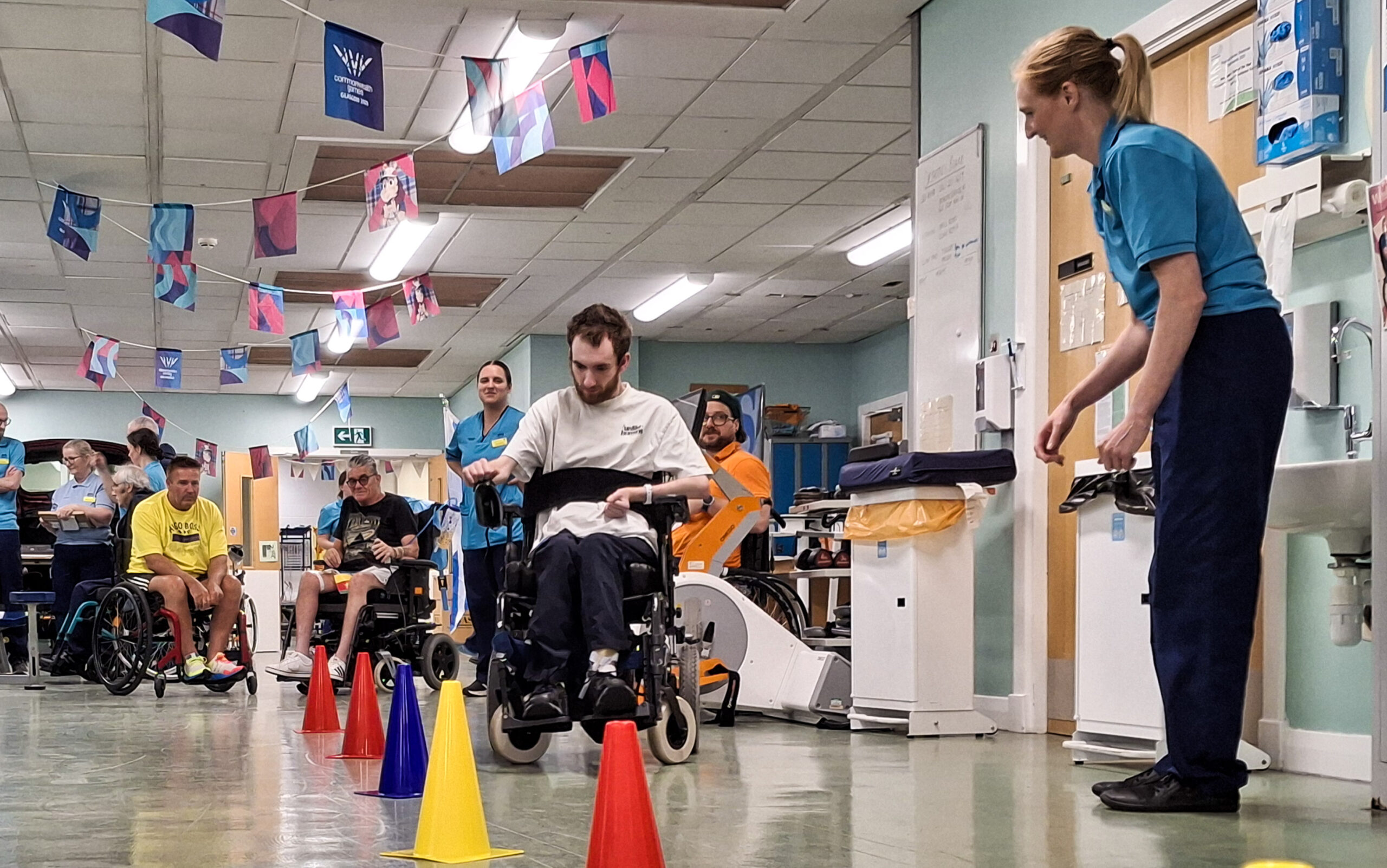 A patient takes part in the wheelchair slalom, supported by fellow patients and staff