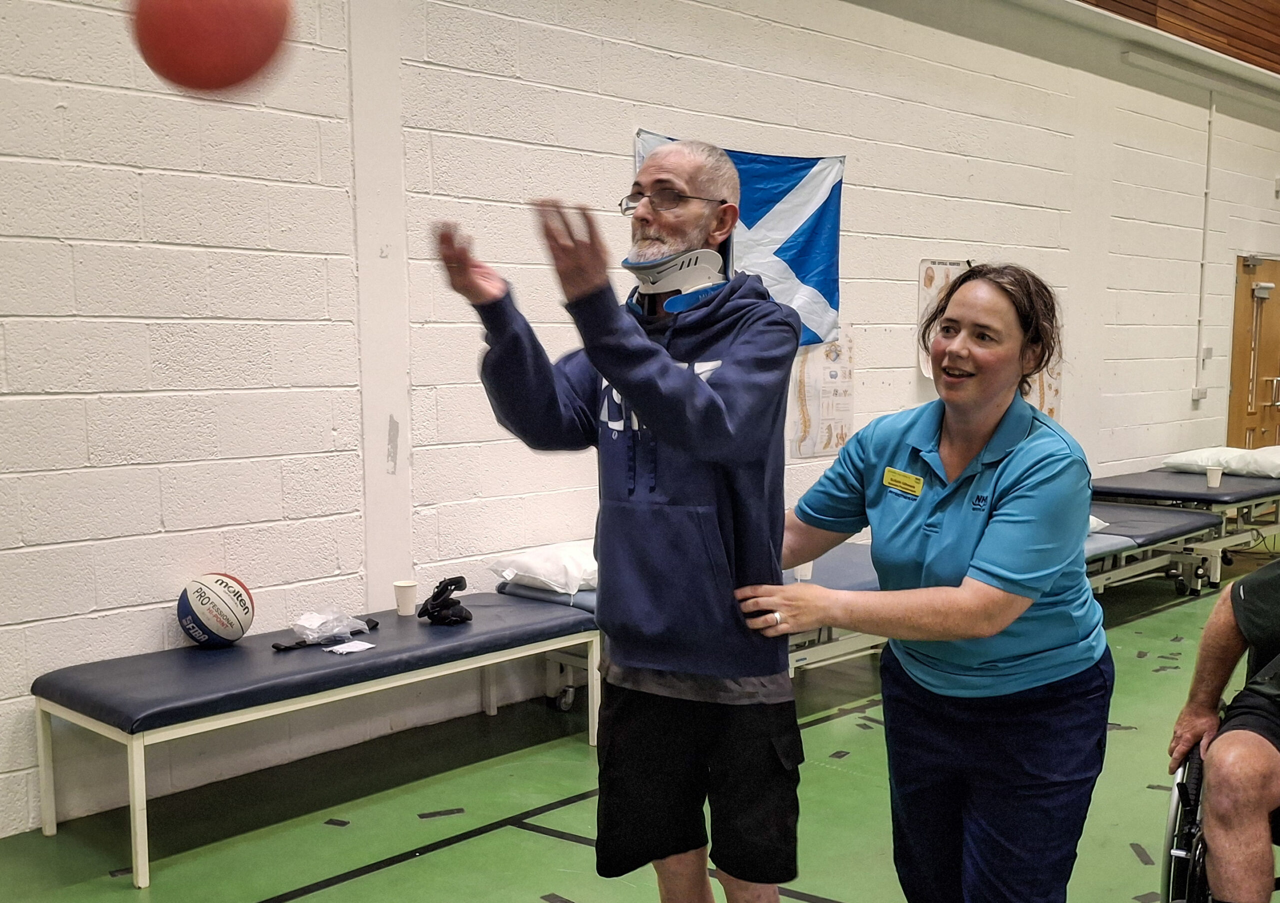 A patient throws a ball in the basketball segment. A staff members supports him