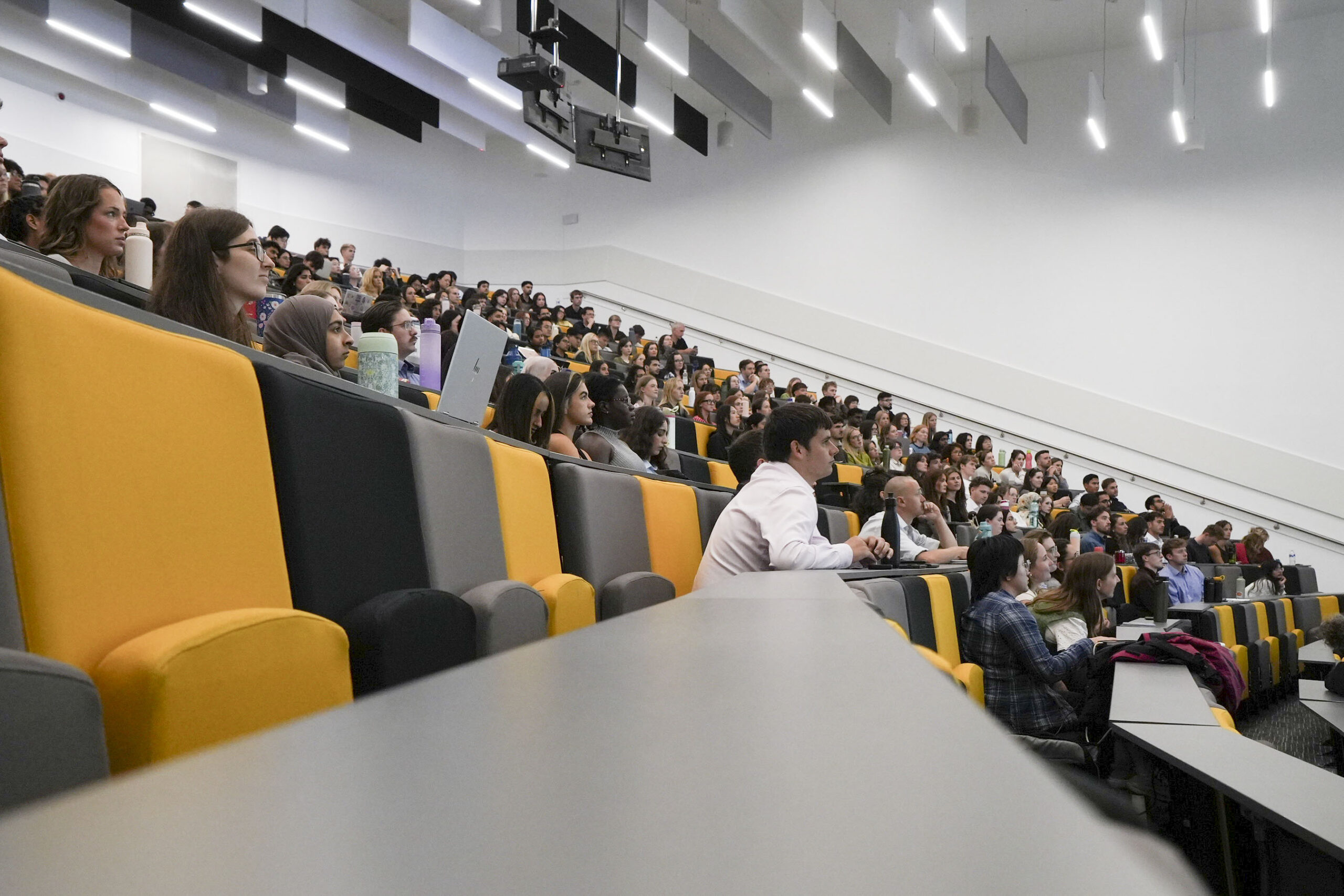 The main lecture theatre, with black and yellow chairs, is full of hundreds of FY1s during one of the information events.