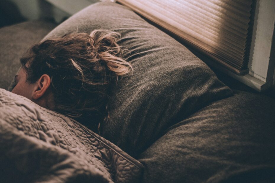 Young person sleeping on her side, with only her head, resting on a brown pillow, visible with the rest her body under brown covers.