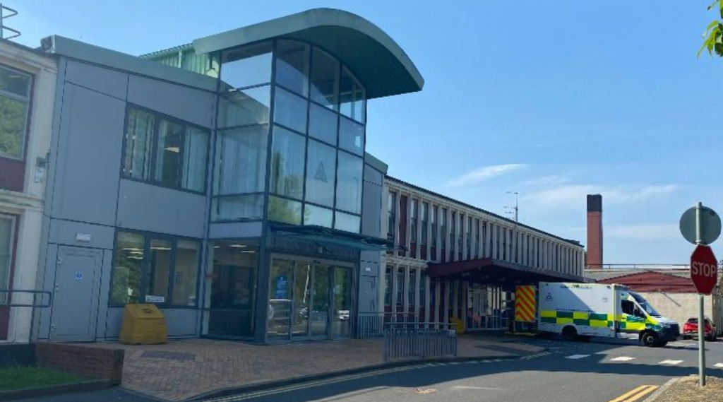External image of the Vale of Leven Hospital entrance, with an ambulance parked at the right and a blue sky