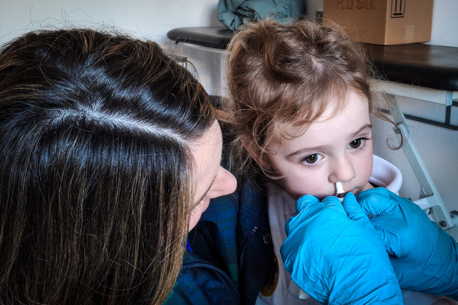 A young girls received the flu vaccine through a nasal spray, with her mother watching carefully
