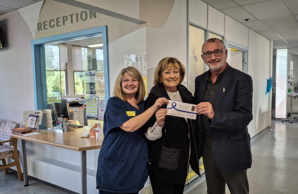 Ethel Smith (centre) holds a queue for £50,000 with Charge Nurse June Raines in uniform on the left and Gerry O'Hare on the right. The picture is taken in front of reception at the Vale of Leven oncology unit.
