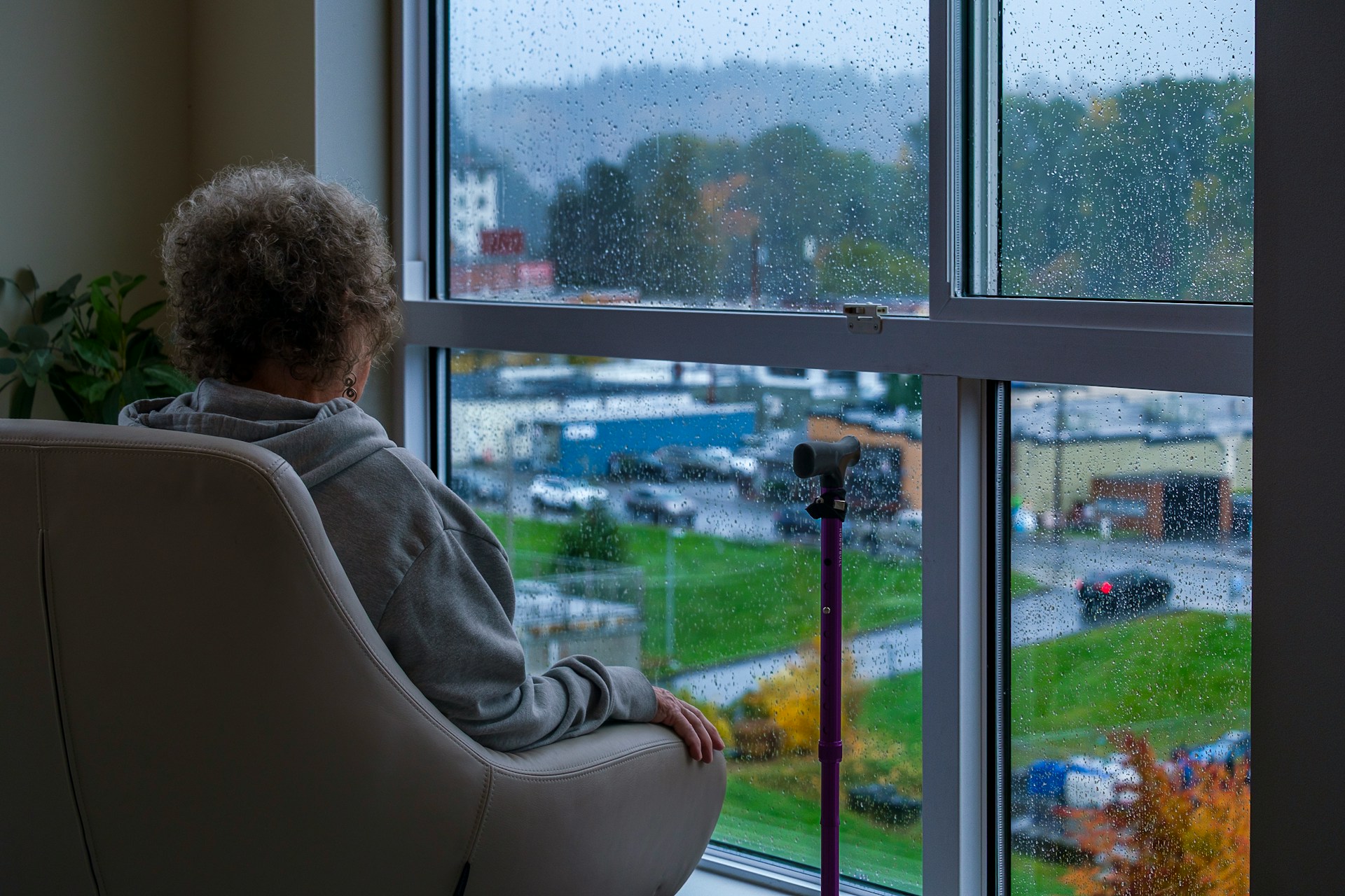 Picture of a woman sitting in a chair looking out of a window that is covered in raindrops